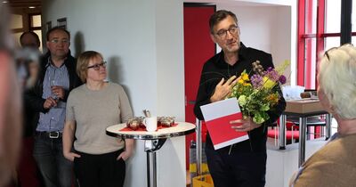 Ein Mann hält eine Mappe und Blumen in der Hand.