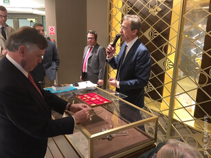 A man with a microphone presents items in a glass display case.
