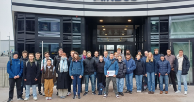 Große Gruppe steht vor dem modernen Glaseingang vom Airbus-Hauptgebäude.