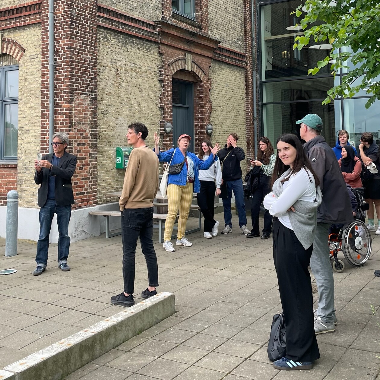 Foto Teilnehmende Zirka 10 Personen stehen vor einem Haus und gucken auf etwas