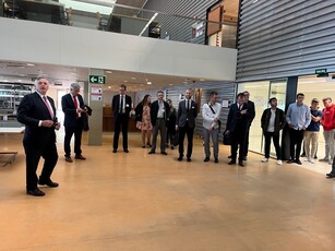 A man in a suit gives a tour to a group in a spacious university lobby.