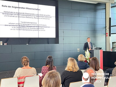 Professor spricht am Pult und Teilnehmende schauen zur Präsentation