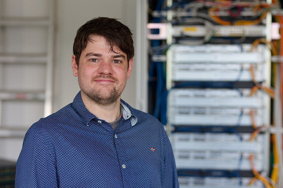 In einem Labor der TH Lübeck steht Sebastian Hauschild vor einem Serverschrank.