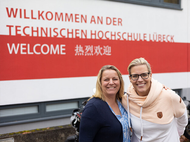 Zwei Frauen stehen vor dem TH Lübeck Schriftzug