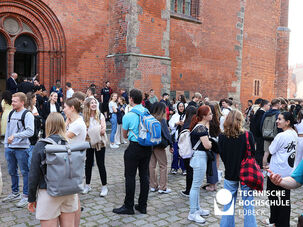 Auf diesem Bild sieht man viele Studierende vor der Kirche stehen, die sich unterhalten 