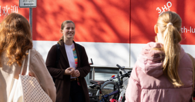 Drei Frauen  Eine Frau im Zentrum die lacht, im Vordergrund Hinterköpfe von zwei anderen Frauen