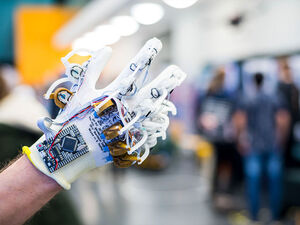 Das Bild zeigt eine Hand, die einen Handschuh zeigt, auf dem verschiedene elektronische Komponenten verarbeitet sind