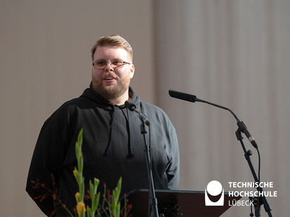 Absolvent hält Abschlussrede Der Absolvent Justin Heim steht in schwarzem Pullover hinter einem Rednerpult