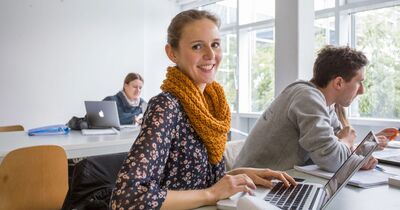 Eine Studentin sitzt in einem Seminarraum am Laptop.
