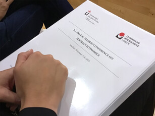 A person holds a white binder for the "3rd Annual Madrid Conference."