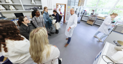 Schülerinnen stehen einem Professor gegenüber der etwas erklärt 