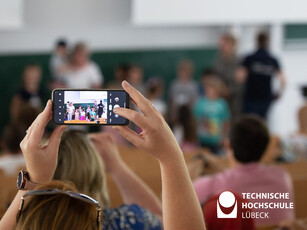 Gewinnerteam wird fotografiert Im Vordergrund ein Handy, im Hintergrund verschwommen eine Gruppe von Kindern, die etwas gewonnen haben