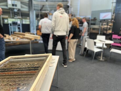 Im Vordergrund ein Ausstellungsstück mit verschiedenen Baumaterialien, dahinter stehen Menschen am Messestand.