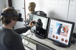 Mann trägt VR BRille und hält mit Messgerät auf ein Kunstgesicht