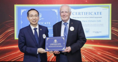 Zwei Personen im Anzug halten gemeinsam eine Urkunde vor einer großen Leinwand mit Zertifikat im Hintergrund.