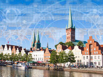 Auf dem Bild sieht man die Petri Kirche und die Trave bei Sonnenschein, in den Himmel sind Grafiken eingearbeitet worden, die für Digitalisierung stehen 