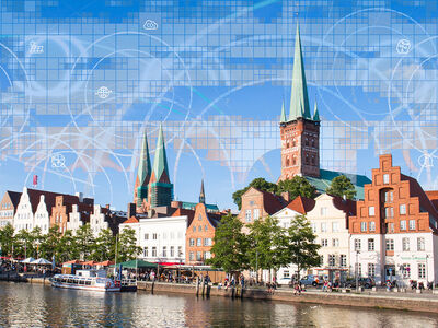 Auf dem Bild sieht man die Petri Kirche und die Trave bei Sonnenschein, in den Himmel sind Grafiken eingearbeitet worden, die für Digitalisierung stehen 