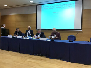 Four men sit at a long table for a panel discussion at a conference.