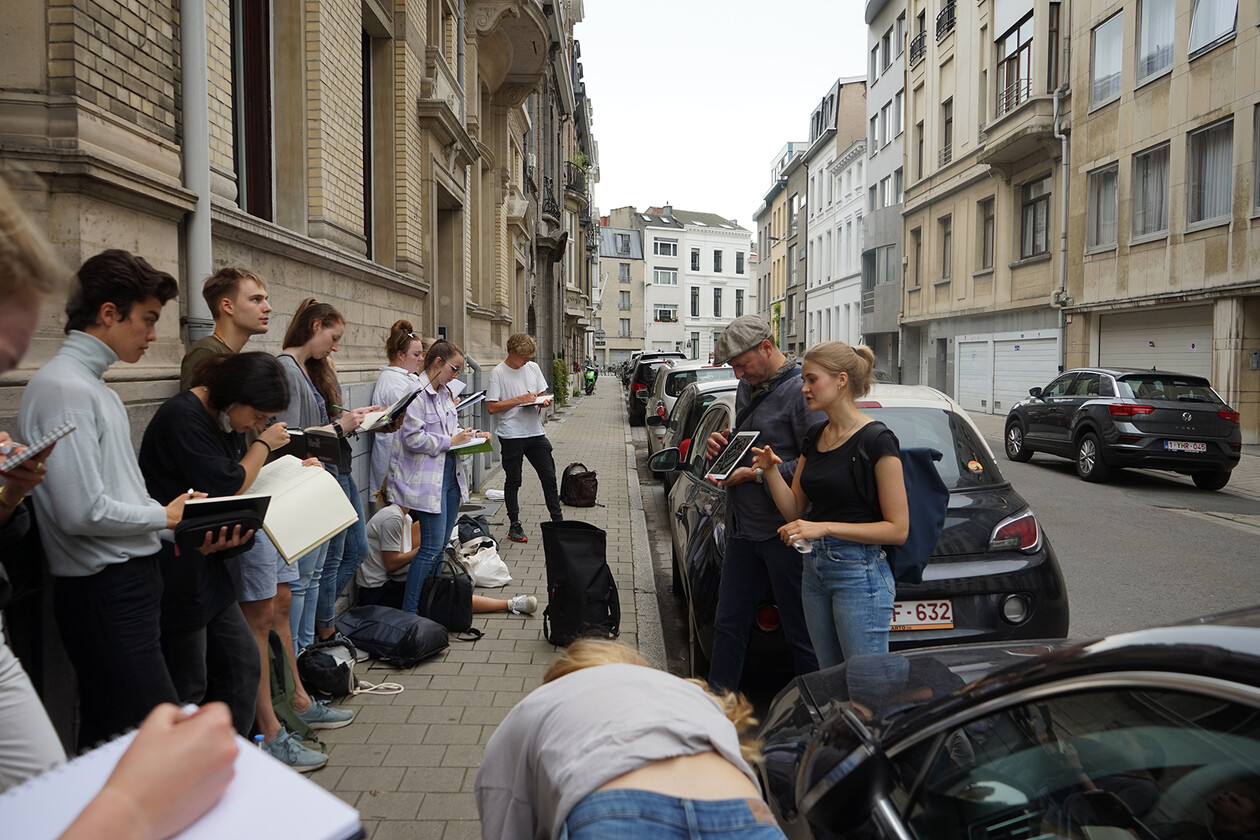 Studierende stehen skizzierend an einer Hauswand in einer städtischen Straße.