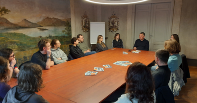 Gruppe sitzt zur Besprechung an einem Tisch in einem Raum mit Wandmalereien.