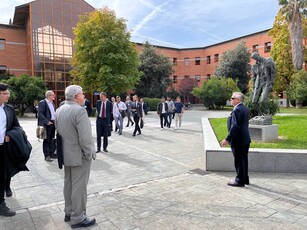 A man in a suit addresses a tour group in a university courtyard.