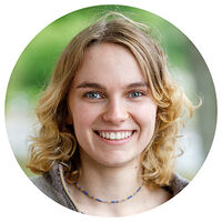 Porträtfoto einer jungen Frau mit lockigem, schulterlangem blondem Haar und blauen Augen, die freundlich lächelt. Sie trägt eine feine blau-goldene Halskette. Das kreisförmig zugeschnittene Bild zeigt sie vor einem unscharfen grünen Hintergrund.
