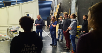 Mann erklärt einer Gruppe Details in einer Kulissenwerkstatt.