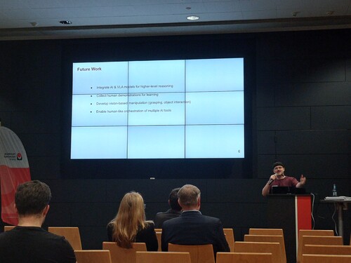 Vortrag mit Folie „Future Work“ zu KI-Forschung im Hörsaal.