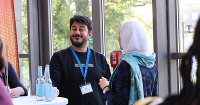 Ein Mann mit einem dunklen Pullover lacht in die Kamera.