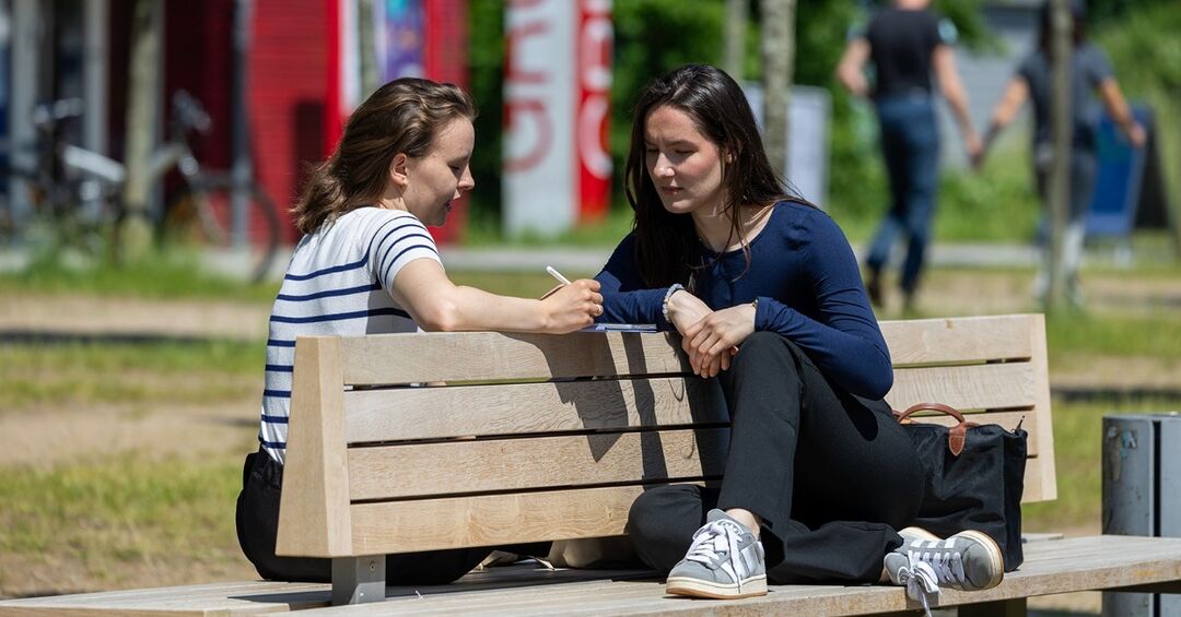 Zwei Studentinnen sitzen auf einer Bank auf dem Campus.