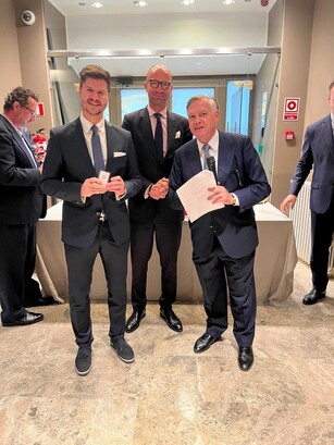 Three men in suits pose for a photo during an awards reception.