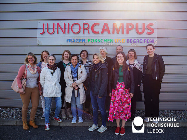 Lehrende stehen vor dem JuniorCampus Schriftzug
