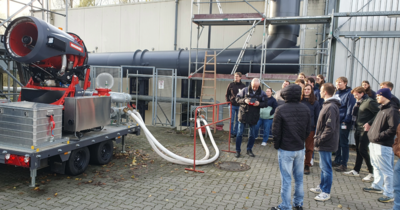 Gruppe betrachtet eine große rote Industriemaschine im Außenbereich.