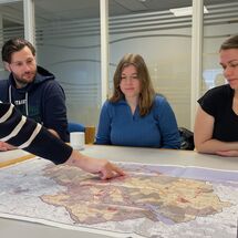 Drei Personen gucken auf eine Landkarte wo eine Hand draufzeigt
