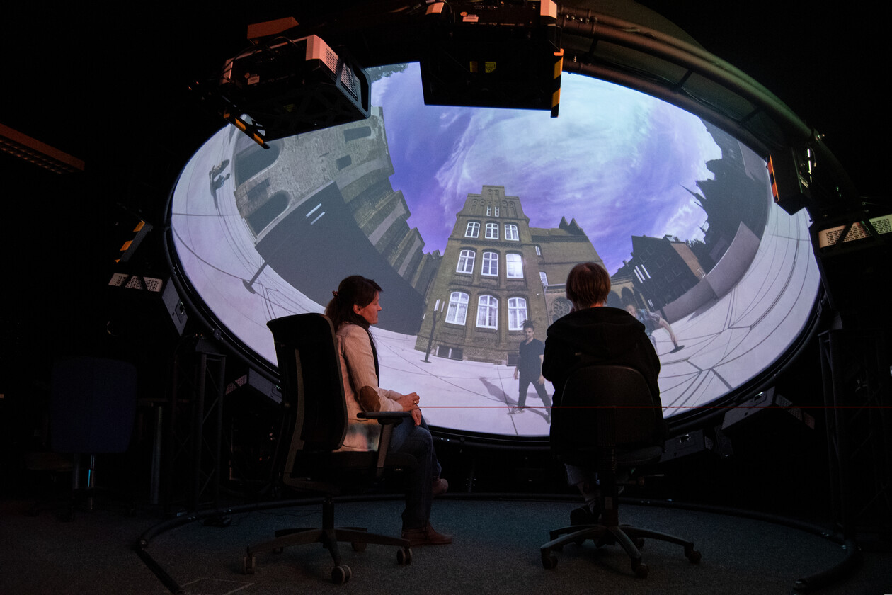 Personen sitzen in einer Kuppel und schauen sich ein 360 Grad Video an, welches auf der Innenseite zu sehen ist.