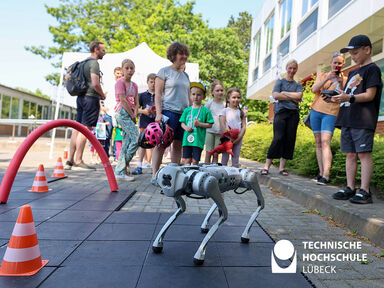 Ein Roboterhund im Vordergrund, der durch einen roten Bogen läuft. Im Hintergrund eine Menschenmenge, die zuschaut. 