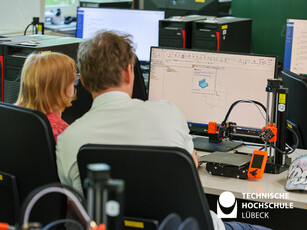 3D Druck Workshop Zwei Menschen von hinten, schauen auf einen Computer, man sieht eine Handystütze in einem 3D-Programm