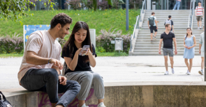 Ein Mann und eine Frau sitzen auf einer Bank und schauen gemeinsam aufs Handy