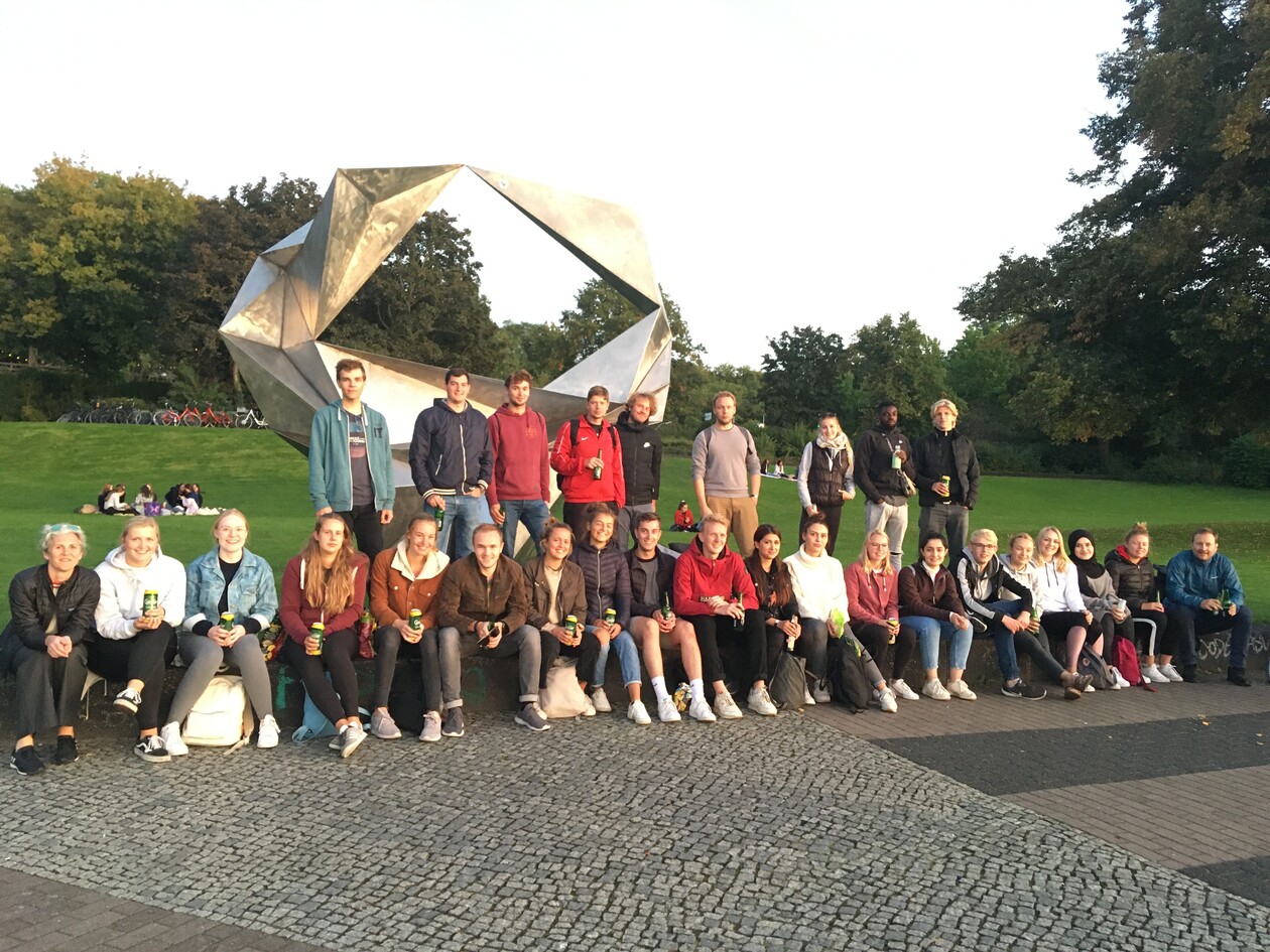 Studierende posieren für ein Gruppenfoto vor einer Metallskulptur im Park.