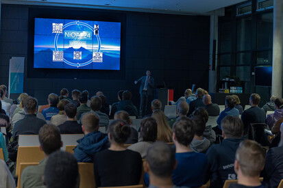 Begrüßung der Teilnehmenden Night of AI Sitzende Teilnehmende gucken auf den vorne stehenden Präsentator