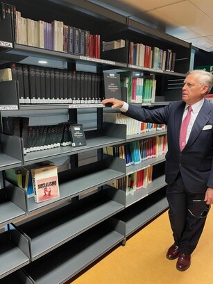 A man in a suit points to a collection of books on a library shelf.