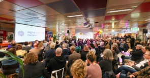 Publikum sitzt vor Leinwand mit Digital Learning Campus Logo und Redner.
