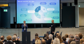 Zwei Männer vor einer Leinwand, die zum Publikum reden