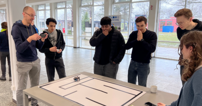 Ein Betreuer filmt den Roboterlauf mit dem Handy, Schüler schauen gebannt zu.