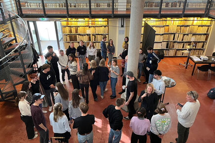 Gruppe von ca. 30 Studierenden bei einer Veranstaltung in einer historischen Bibliothek mit raumhohen Bücherregalen und Wendeltreppe – Studiopräsentation oder Workshopsituation im Rahmen eines Lehrprojekts