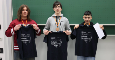 Drei stolze Gewinner präsentieren ihre dunkelblauen Wettbewerbs-Shirts.