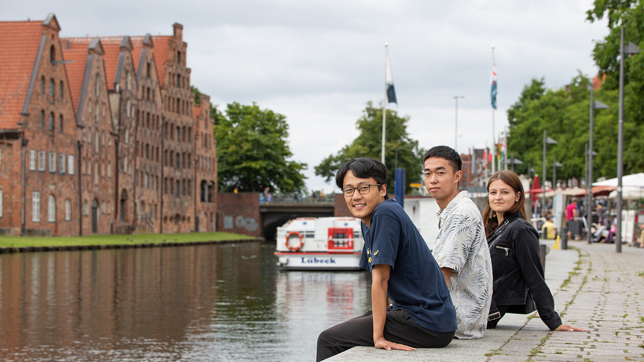 Three students sitting relaxed on the quay wall facing the old town.
