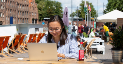 Eine Frau sitzt vor einen Laptop, im Hintergrund die Altstadt von Lübeck