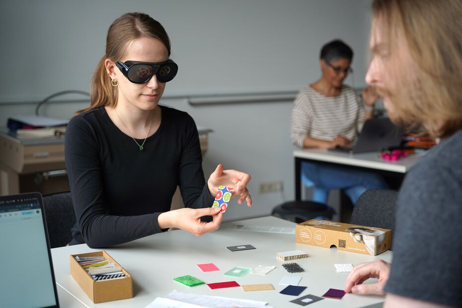 Eine Studierende testet mehrere verschiedene Oberflächen und hat dabei eine Brille auf, die die Sicht einschränkt.