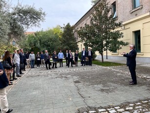 A man in a suit gestures while speaking to a tour group in a courtyard.